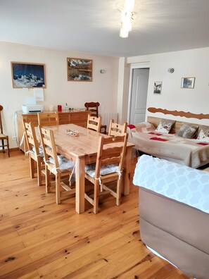 A room with a wooden dining table, chairs, a sofa, and a bed. - Gîte 'Notre Désir' with Mountain View, Private Terrace and Wi-Fi (Abriès-Ristolas)
