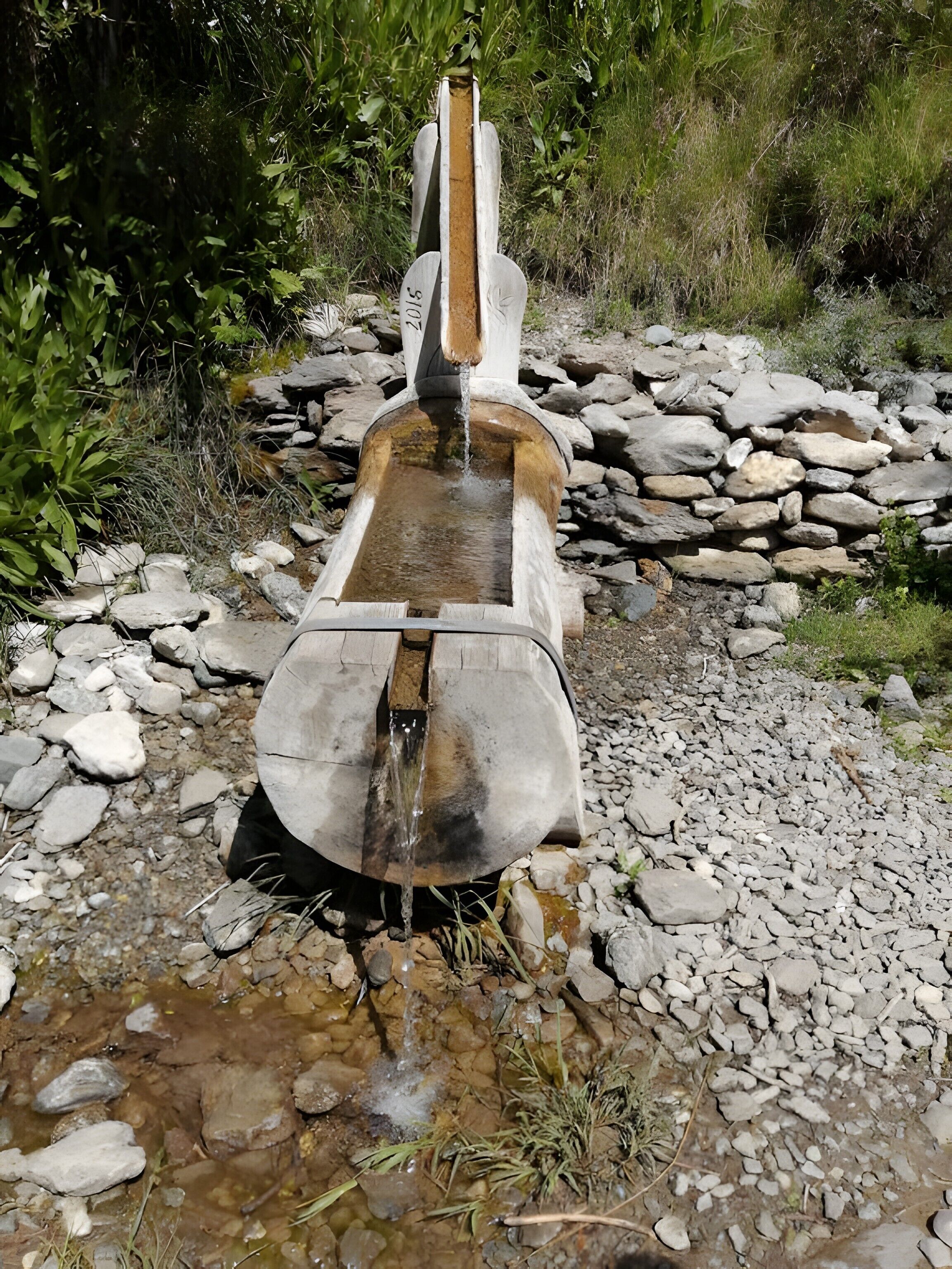 Una fuente de piedra rústica con estructura de madera, rodeada de rocas y follaje.