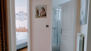 A room with a wooden floor, a bed, a shower, and a door leading to another room. - Gîte 'Notre Désir' with Mountain View, Private Terrace and Wi-Fi (Abriès-Ristolas)