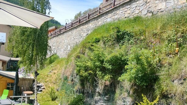A hillside building with a balcony, surrounded by greenery and a stone wall. - Gîte 'Notre Désir' with Mountain View, Private Terrace and Wi-Fi (Abriès-Ristolas)