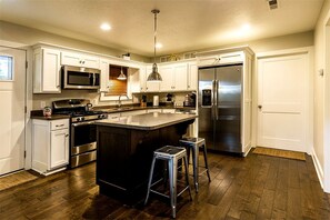 A modern kitchen with white cabinetry, stainless steel appliances, a central island with stools, and a wooden floor. - Sweet Private Cabin with Jacuzzi and Fire Pit in Ohio (Sugarcreek)