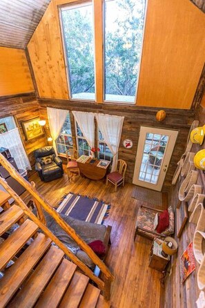 A wooden cabin interior with a loft bedroom, a dining area, and a staircase.