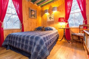 A wooden room with a bed, a chair, a table, and a window with curtains.