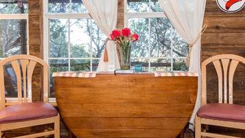 A wooden table with chairs, a vase of red flowers, and a window with curtains.