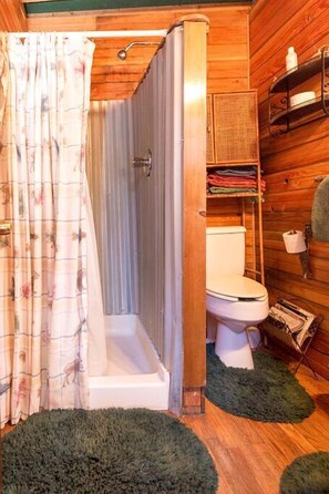 A wooden cabin bathroom with a shower, toilet, and shelves with towels.