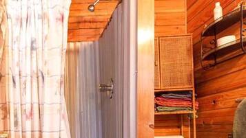 A wooden cabin bathroom with a shower, toilet, and shelves with towels.
