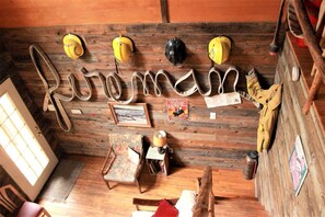 Une pièce rustique avec des murs en bois, un plancher en bois, un lit, une chaise, une table et un porte-manteau avec des chapeaux.