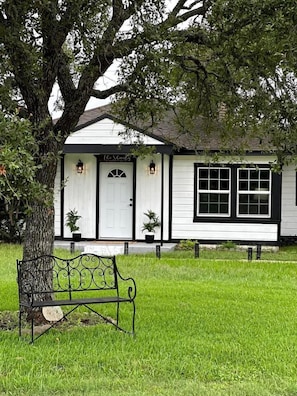 A white building with a black door, two potted plants, and a bench in front.