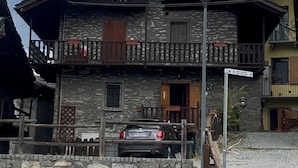 A stone building with a wooden balcony, a car parked in front, and a sign indicating a direction. - Chalet in the Village of Charvensod - Relaxation and Nature (Charvensod)