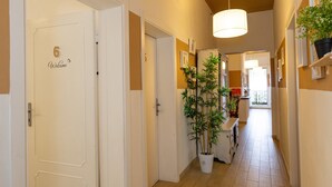Un pasillo con una puerta marcada '6 Welcome', una planta en maceta y un aplique.