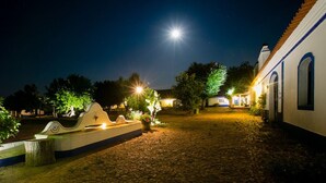 Une cour pavée de pierres, agrémentée d’une fontaine, illuminée par des lampadaires et la pleine lune.
