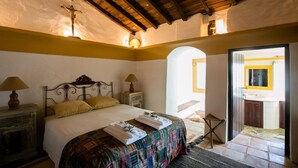 Une chambre à coucher avec un lit, des lampes de chevet, un plafond en bois et une porte donnant sur une salle de bain.