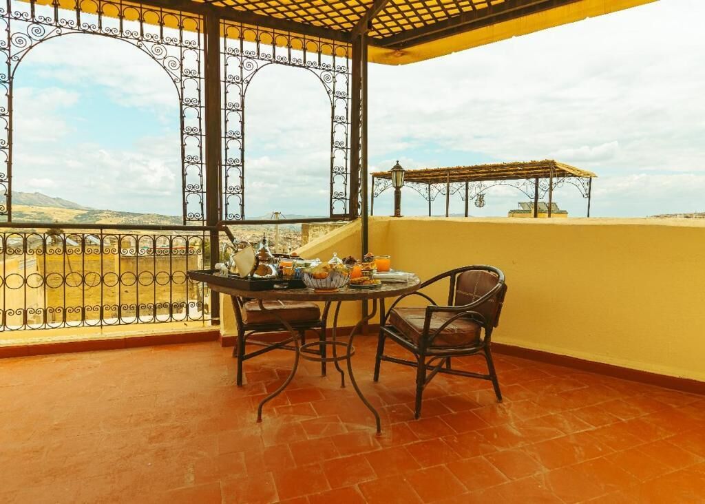A balcony with a table set for breakfast, chairs, and a view of the countryside.