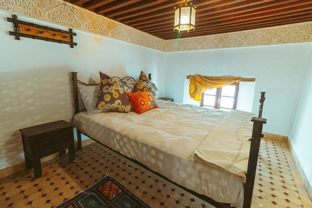 A bedroom with a bed, a nightstand, a patterned rug, and a decorative wall piece.
