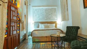 Ein Schlafzimmer mit einem Bett, einem kleinen runden Tisch, einem Sessel und einem gemusterten Boden.