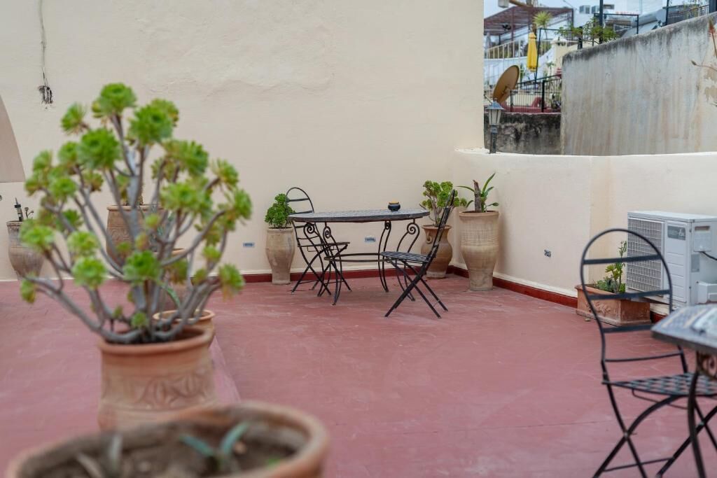 Um terraço no telhado com uma mesa redonda e cadeiras, rodeado por plantas em vasos.