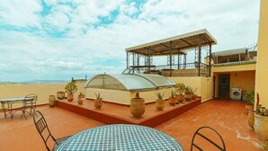 A rooftop terrace with a round table, chairs, potted plants, a pergola, and a view of the landscape. - Riad Dar Kenza (Fes)
