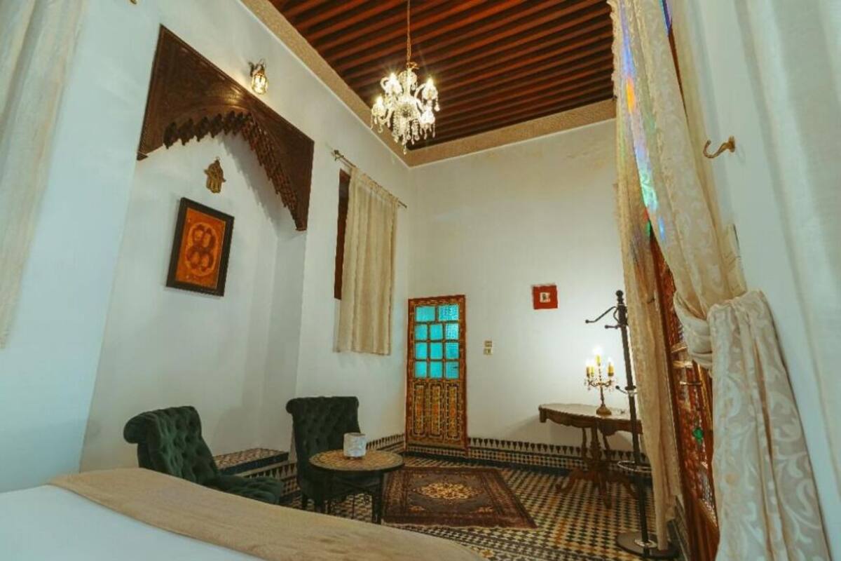 A traditional room with a patterned floor, a chandelier, a wooden door with glass panels, and two chairs.
