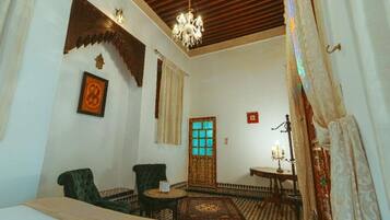 A traditional room with a patterned floor, a chandelier, a wooden door with glass panels, and two chairs.