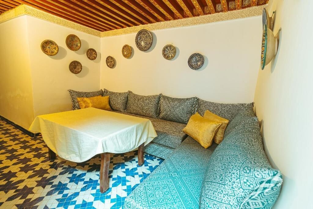 A cozy room with a patterned sofa, a small table with a white tablecloth, and decorative plates on the wall.