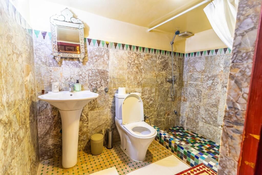 A bathroom with a marble wall, a pedestal sink, a toilet, and a shower.