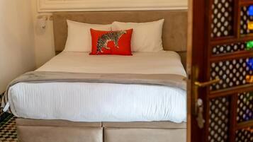 Un letto con una testiera beige, biancheria da letto bianca e un cuscino rosso con effetto leopardo.
