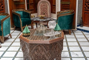 Quarto tradicional com mobiliário ornamentado, chão em mosaico de mármore e uma mesa central com objetos decorativos.