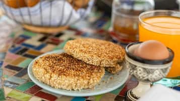 Une assiette contenant deux aliments, un verre de jus d’orange et un petit bol avec un œuf, le tout posé sur une table colorée recouverte de carreaux.