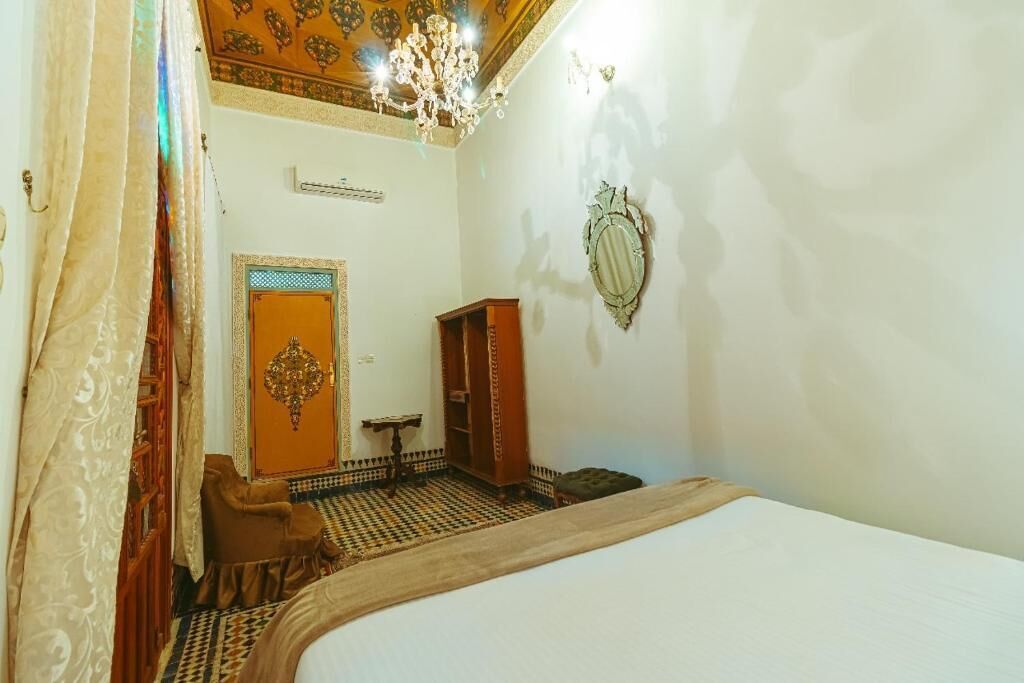 A room with a bed, a wooden cabinet, a small table, a chair, and a patterned floor.