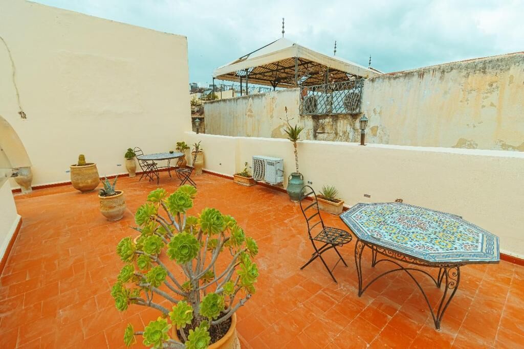 Una terraza en la azotea con mesa y sillas, plantas en macetas y una pérgola.