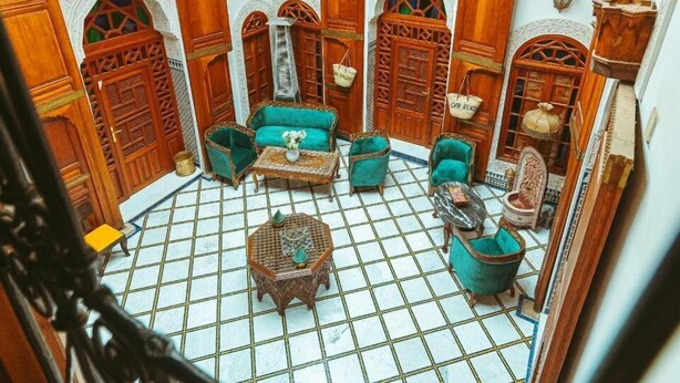 A traditional Moroccan interior with ornate wooden doors, a tiled floor, and a seating area with cushions and a small table. - Riad Dar Kenza (Fes)