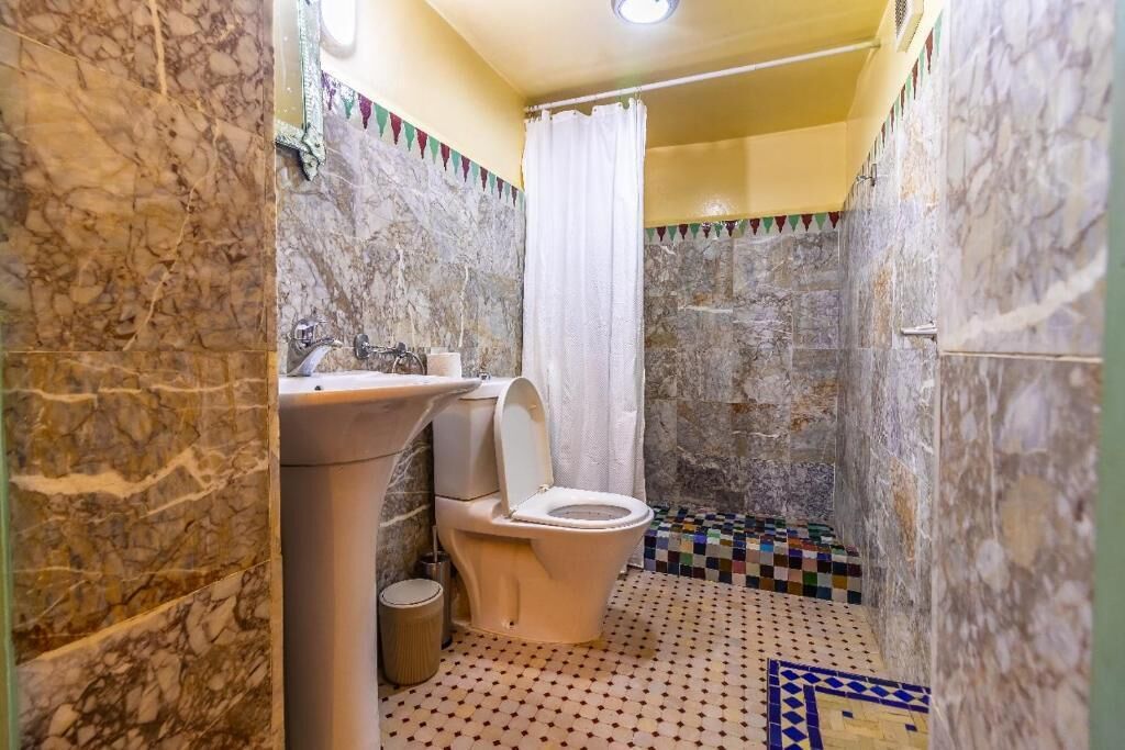 Een badkamer met een marmeren wand, een toilet, een wastafel en een douche.