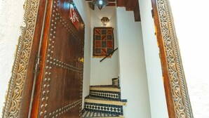 A staircase with patterned tiles leading to a room with a patterned window and a decorative ceiling light. - Riad Dar Kenza (Fes)