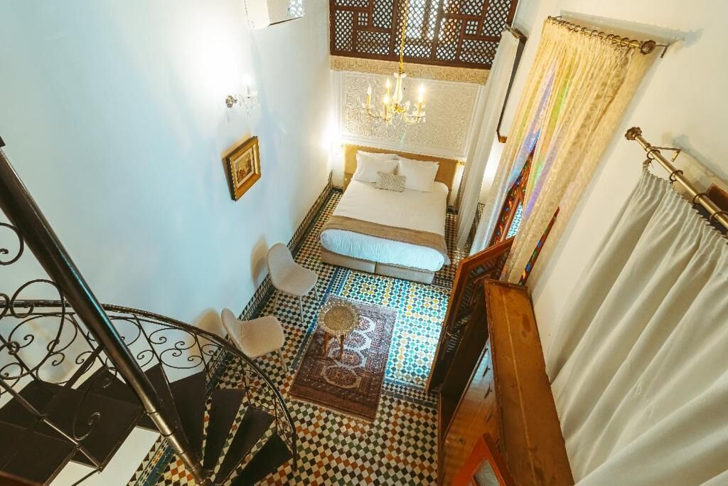 A bedroom with a checkered floor, a bed, a chandelier, and a staircase.