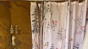 A bathroom with a shower curtain featuring a nature print, a wooden wall, and a shelf with toiletries. - Spacious Tipi with Outdoor BBQ and Fire Pit in Texas (Marble Falls)