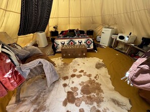 Une pièce aménagée avec une tente, un lit, une petite table, une valise et un tapis en peau de vache.