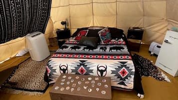 A tented room with a bed, a small table, a heater, and a storage box.