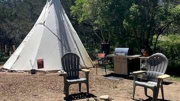Un tipi con dos sillas y una hoguera en un área boscosa.