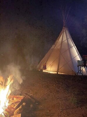 A teepee with a fire in front, surrounded by a dirt ground.