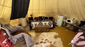 Ett rum med tältduk som väggar, en säng, ett litet bord, en resväska och en matta gjord av kohud.