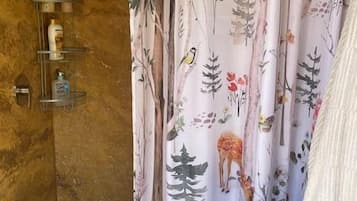 Een badkamer met een douchegordijn met een natuurprint, een houten wand en een plank met toiletartikelen.