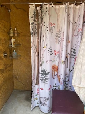 A bathroom with a shower curtain featuring a nature print, a wooden wall, and a shelf with toiletries. - Spacious Tipi with Outdoor BBQ and Fire Pit in Texas (Marble Falls)