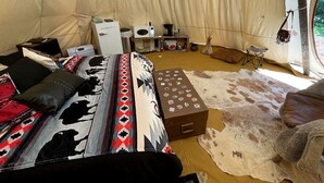 A tent interior with a bed, a small table, a white appliance, and a cowhide rug. - Spacious Tipi with Outdoor BBQ and Fire Pit in Texas (Marble Falls)