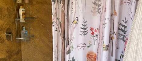 A bathroom with a shower curtain featuring a nature print, a wooden wall, and a shelf with toiletries.