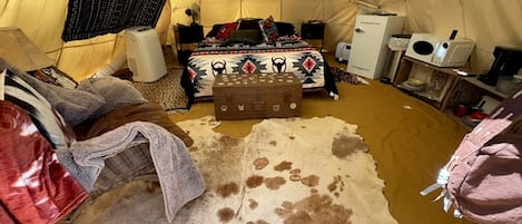 A tented room with a bed, a small table, a suitcase, and a cowhide rug.