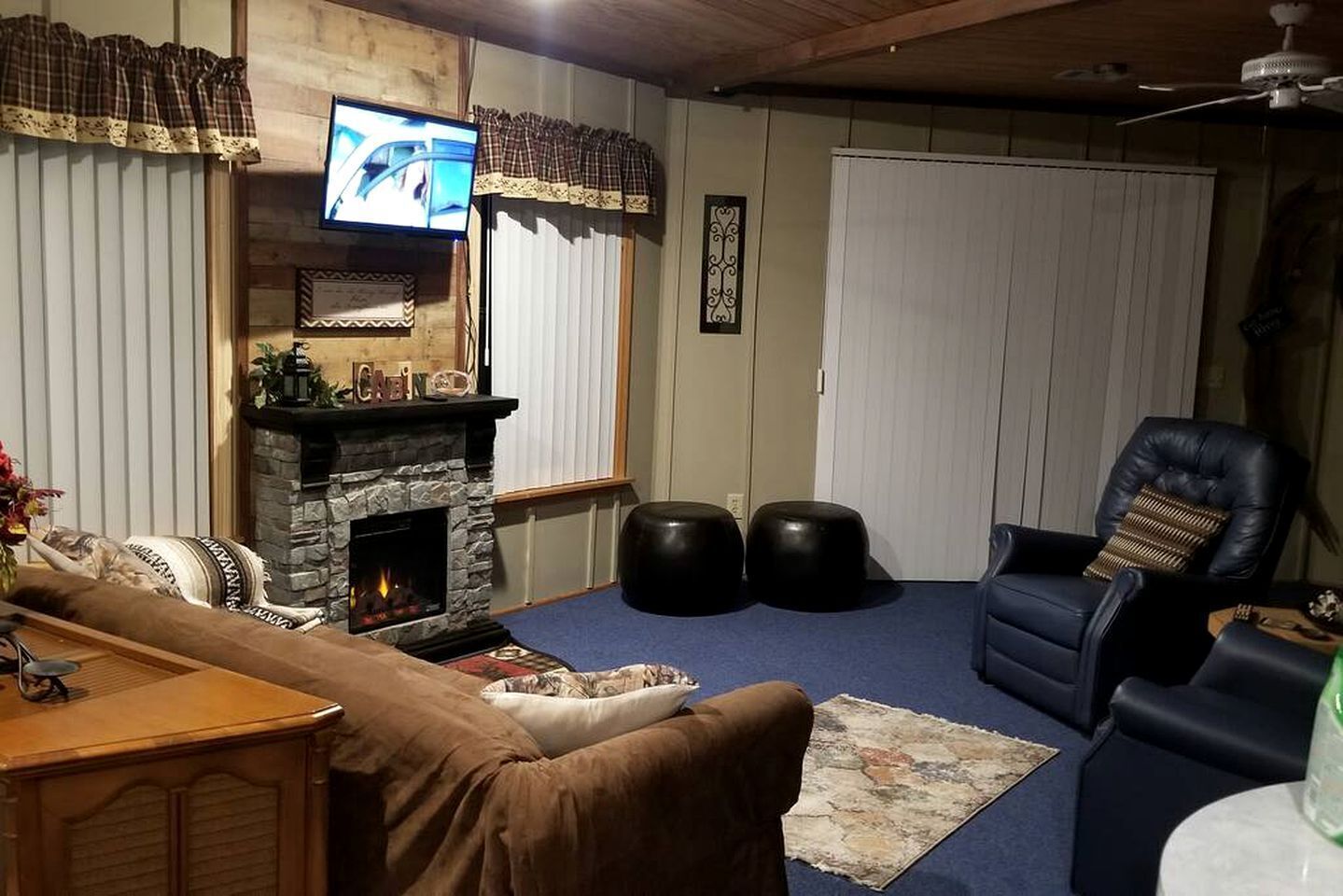 A living room with a stone fireplace, a television mounted above it, a leather armchair, and a blue carpet.