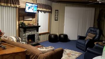 A living room with a stone fireplace, a television mounted above it, a leather armchair, and a blue carpet.