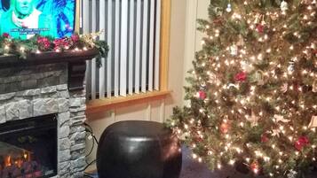 Ein Kamin mit Steinumbauung, ein Weihnachtsbaum mit Lichterkette und Dekorationen sowie ein Fernseher, der ein weihnachtliches Bild zeigt.