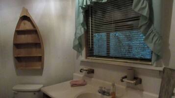A bathroom with a toilet, a sink, a mirror, and a window with blinds.