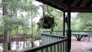 A wooden deck with a hanging plant, surrounded by a forested area and a body of water.